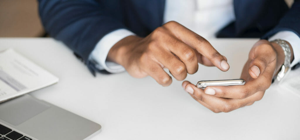 Een close-up van een persoon die aan kennismanagement werkt met een mobiele telefoon in de hand en een laptop op tafel.