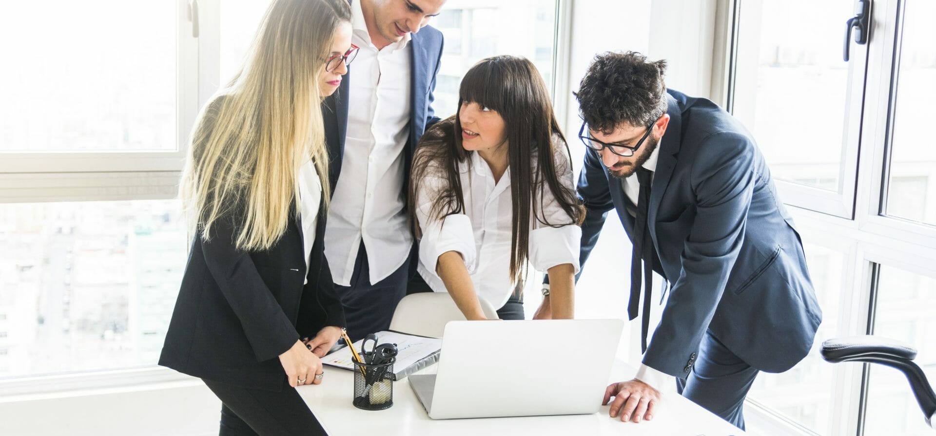 4 Personen, die das 70:20:10-Modell anwenden, stehen vor einem Schreibtisch mit einem Laptop. Eine Person deutet auf den Laptop-Bildschirm.