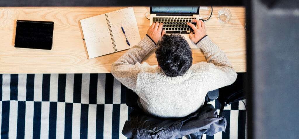 Een persoon zit aan tafel met een laptop, een schrijfblok en een glas, hij gebruikt het À la carte-leermodel voor blended learning.