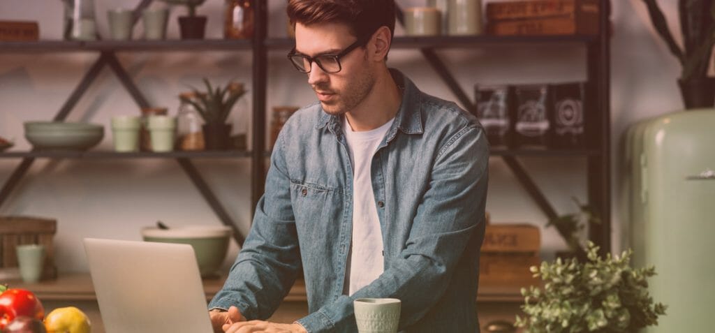 Un homme portant des lunettes utilise un ordinateur portable dans sa cuisine.