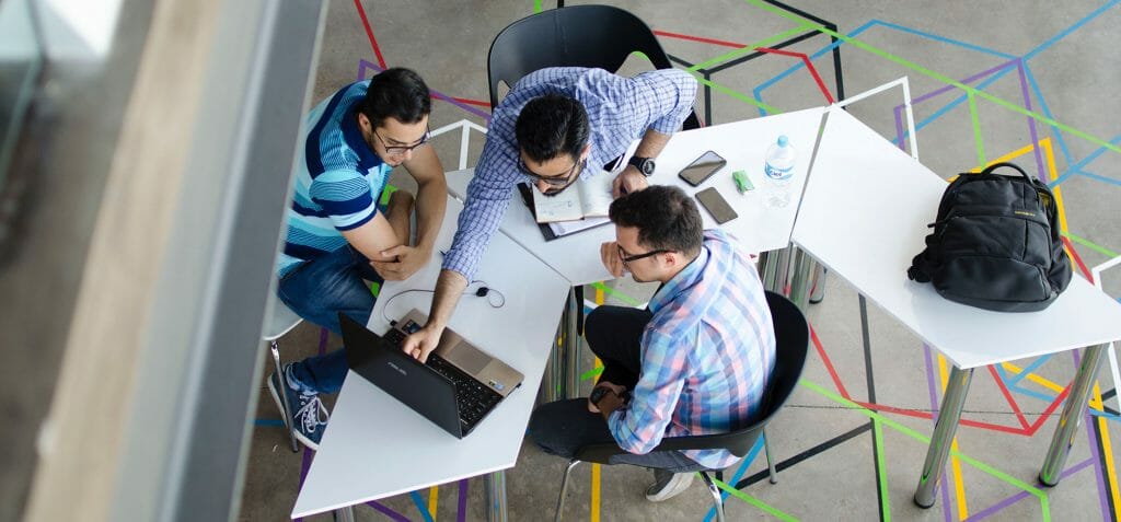 3 personnes assises autour d'une table avec un ordinateur portable et un carnet collaborant sur des cours SCORM et AICC.