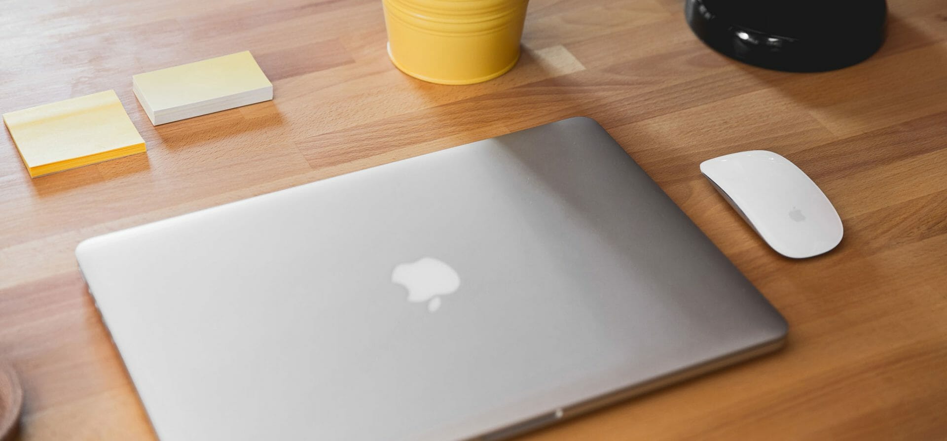 Een tafel met een Mac-laptop, een muis en twee stapeltjes sticky notes.