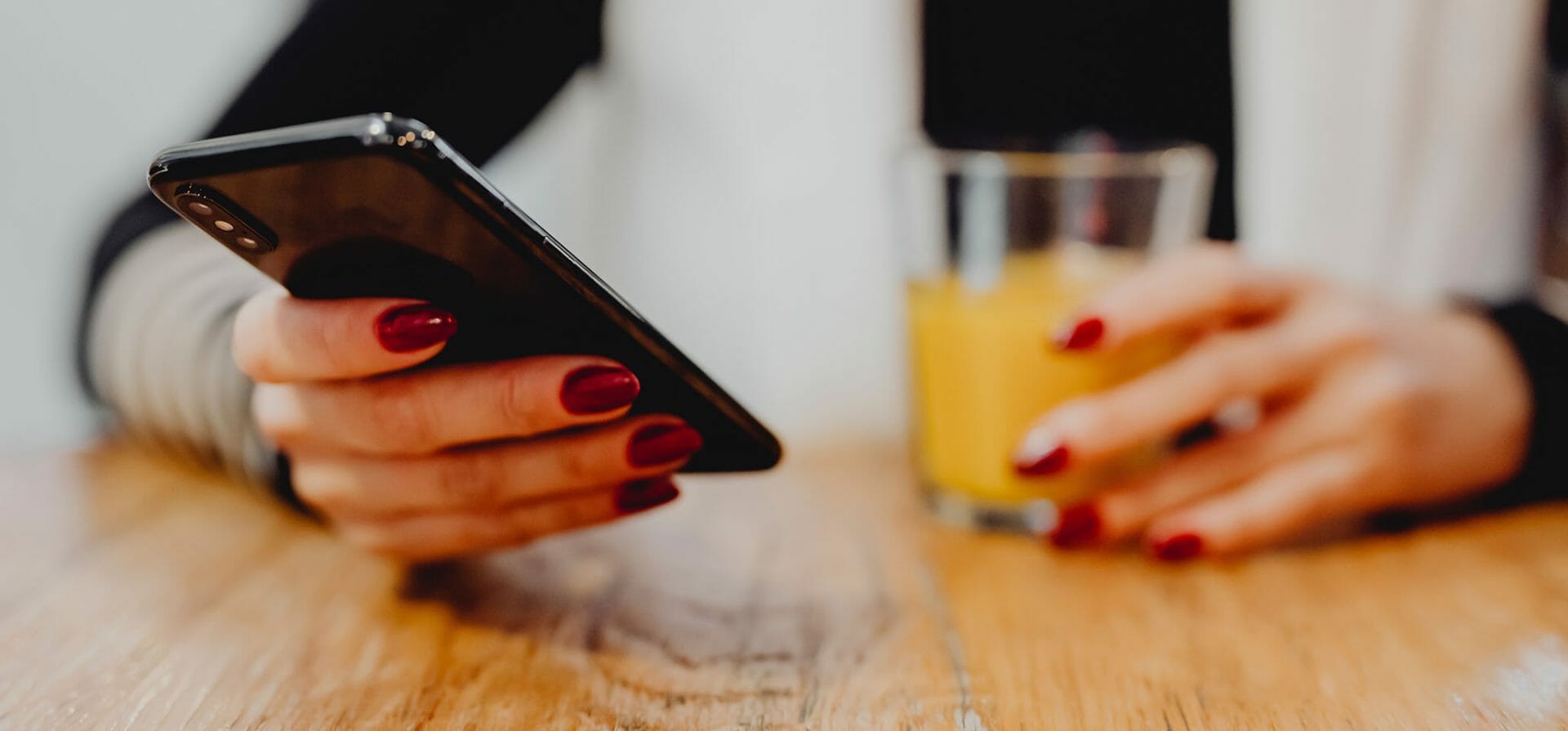 Een persoon zit aan tafel met een glas drinken en gebruikt een mobiele telefoon voor microlearning.