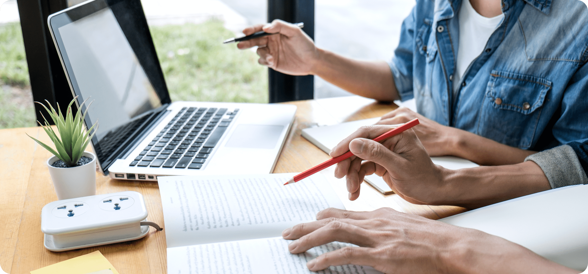 Zwei Personen teilen sich einen Tisch mit Laptops, Papieren und teilen Wissen.