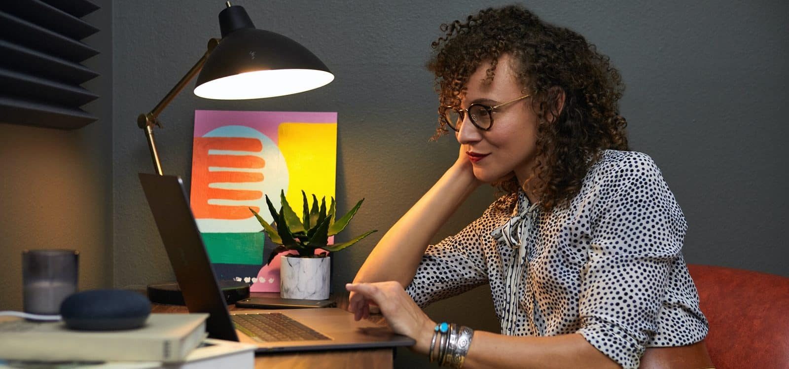 Een persoon die gamification gebruikt voor e-learning, zittend aan een bureau met een laptop, een lamp, een kamerplant en een schilderij op de achtergrond.