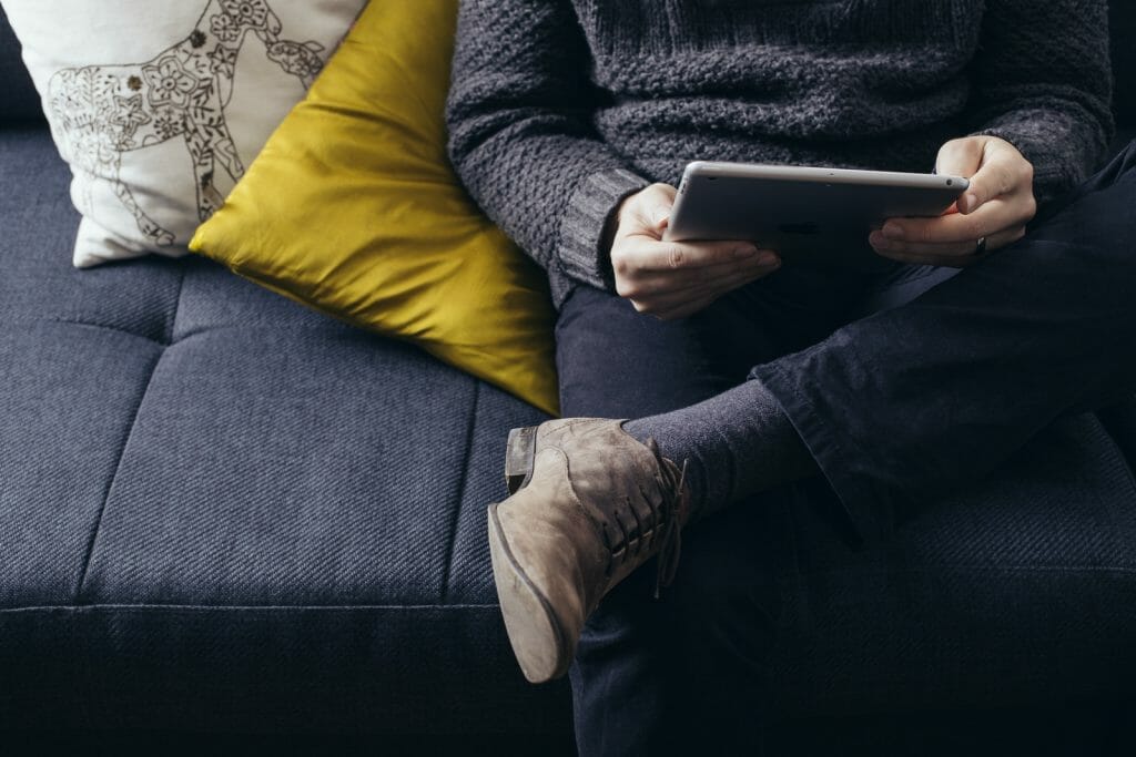 Personne assise sur un canapé suivant une formation vidéo sur une tablette.