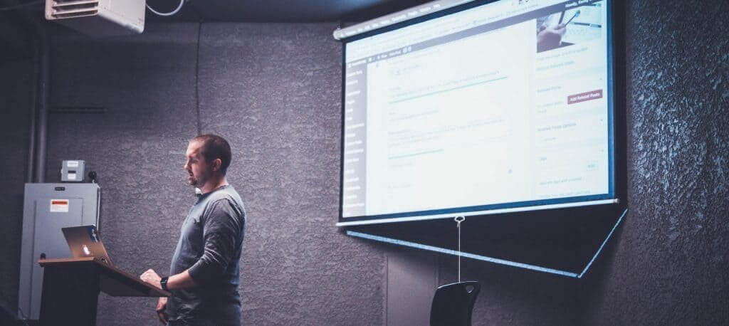 Ein Mann präsentiert eine PowerPoint-Präsentation auf einer Projektorleinwand.