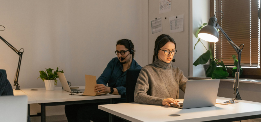 In a modern office setting, people are working at desks with laptops and headsets, focusing on how to make online courses more interactive.