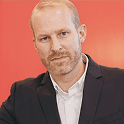 Professional man in a suit with a confident expression against a red background.